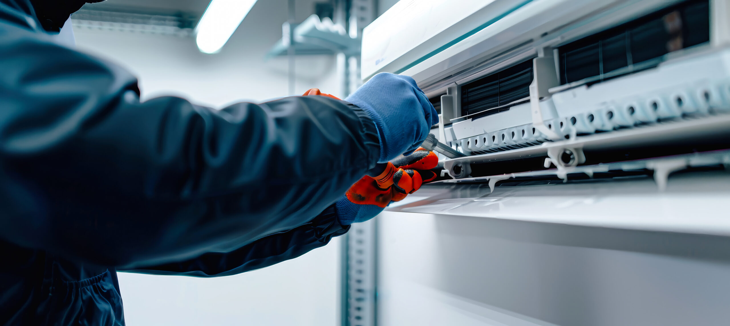 Close-up of a technician's gloved hands cleaning the fresh air grille of an indoor cassette mini-split air conditioner unit.